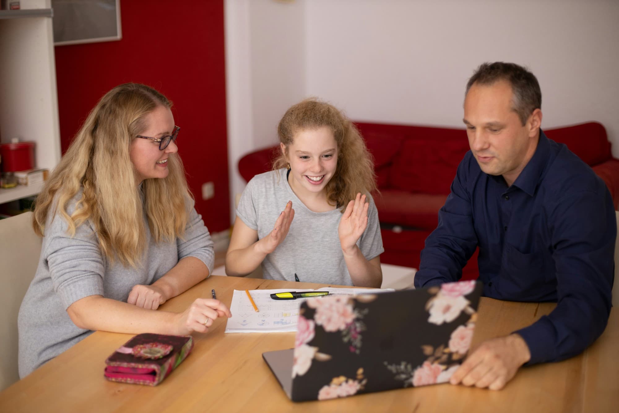 Deux parents souriants aidant leur fille adolescente à faire ses devoirs autour d'un ordinateur portable